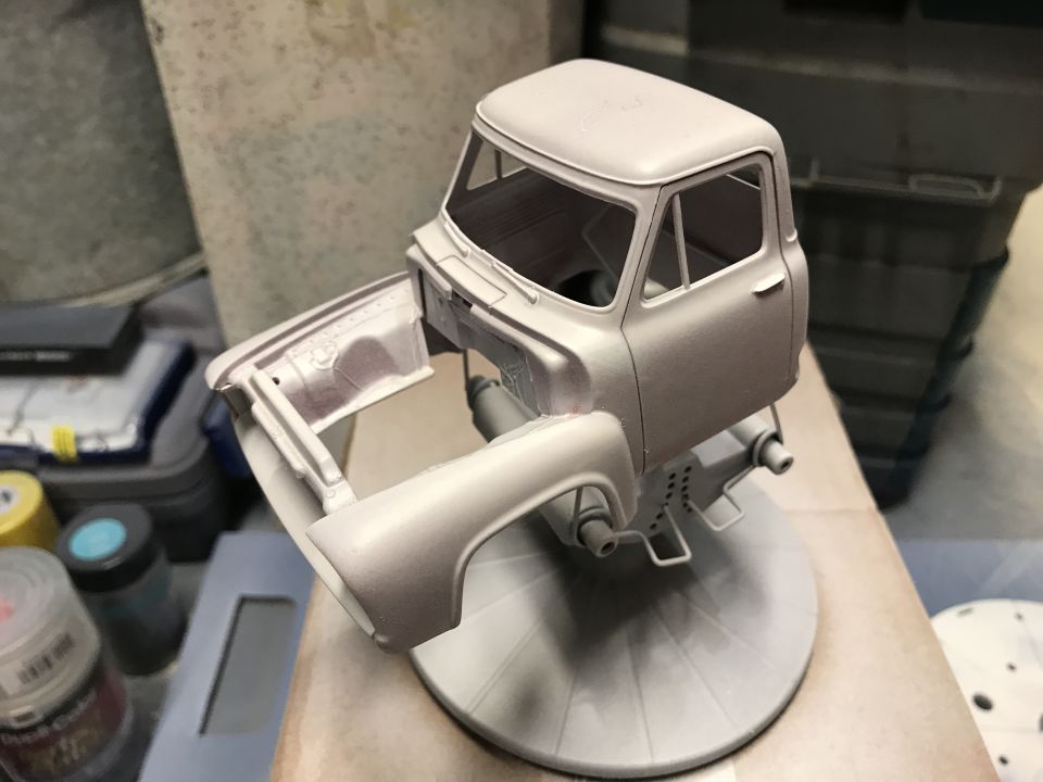 Model truck cab and front fender assembly in light gray primer on a stand.