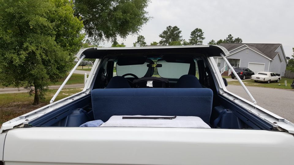 Rear interior of a white 1995 Ford Bronco with blue seats, parked outside a house.