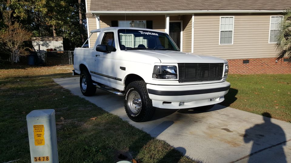 White 1995 Ford Bronco parked in front of a house, with a Tropicana banner on the windshield.