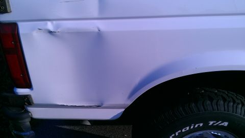 1995 Ford Bronco - A white SUV's rear quarter panel shows damage. The vehicle is seen from the side.