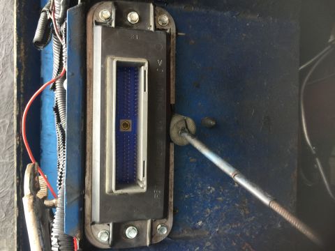 1974 Ford Bronco - Close-up view of an engine control module connector, showing blue pins and a metal rod inserted into a grommet.