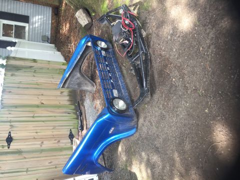 1974 Ford Bronco - Disassembled blue fender and grille assembly, likely for a 1974 Ford Bronco, sits on the ground.