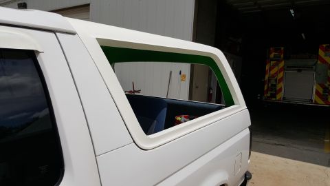 1995 Ford Bronco - The rear window frame of a white SUV is visible, with a hint of blue interior and a fire truck in the background.