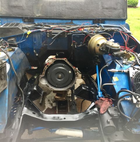 1974 Ford Bronco - The engine bay of a blue vehicle is shown with the transmission removed, revealing the engine block and associated components.