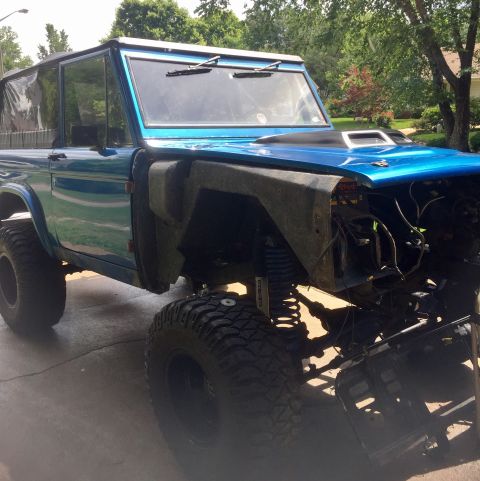 1974 Ford Bronco - A blue 1974 Ford Bronco is shown with a lifted suspension and a missing front fender, indicating it is undergoing modifications.