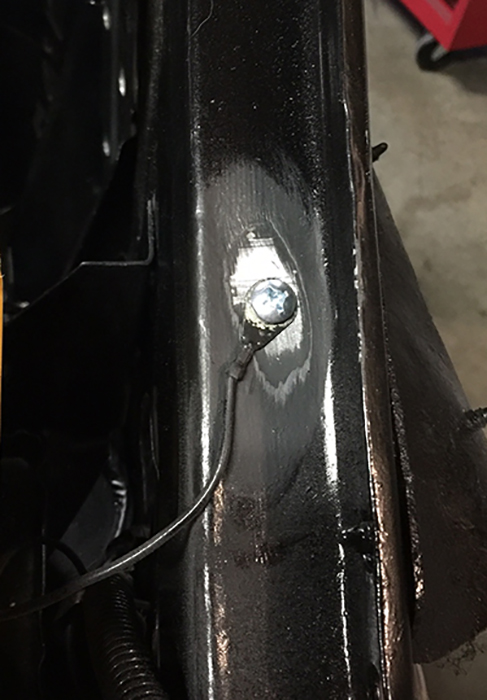 Close-up of a black metal frame with a bolt and attached wire. A black corrugated conduit is visible below