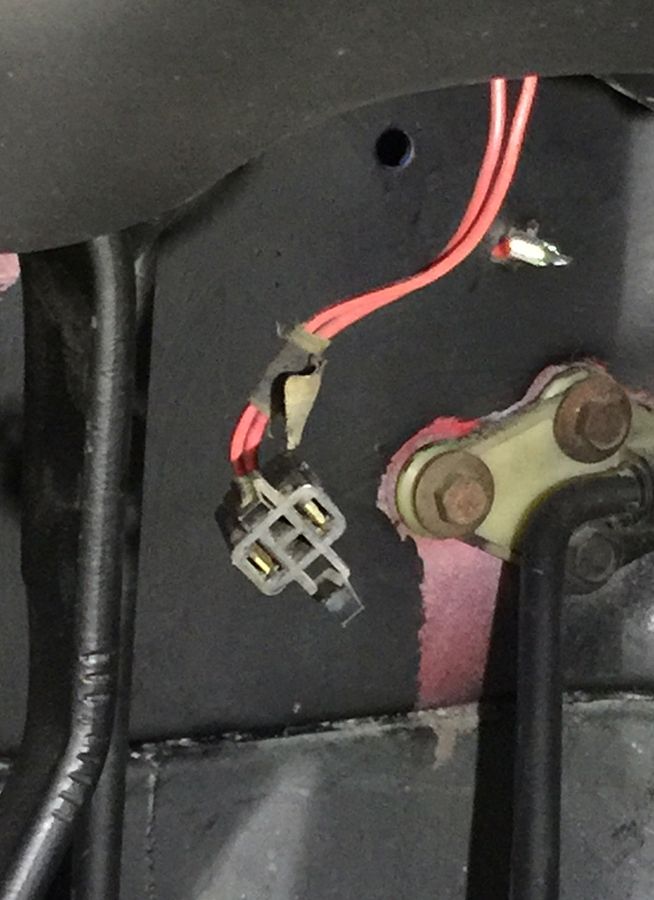 Close-up of a disconnected electrical connector with red wires attached to a black bracket