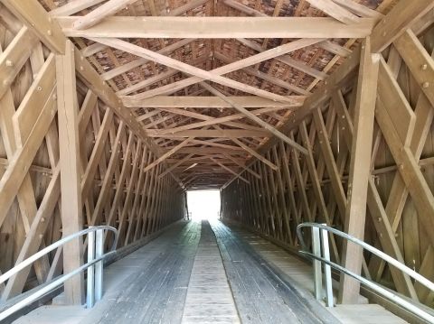 1978 Ford Bronco - The interior of a wooden covered bridge shows its intricate beam and roof construction leading to daylight.