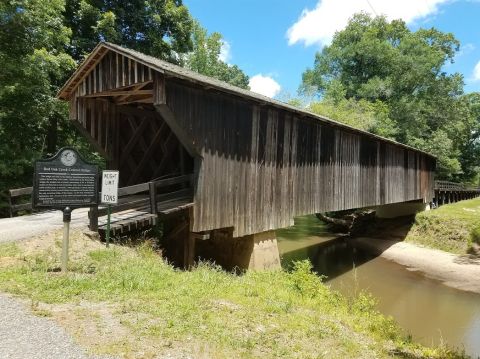 1978 Ford Bronco - A wooden covered bridge spans a calm creek, with a historical marker providing information about its past.
