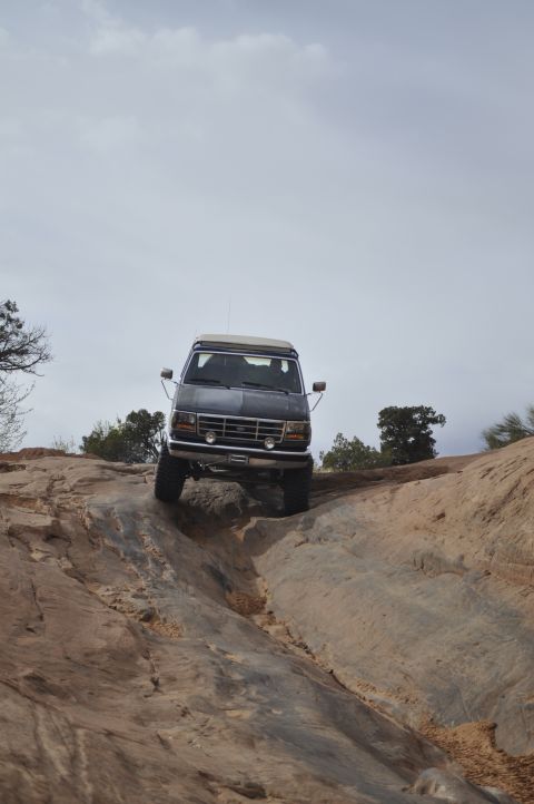 1991 Ford Bronco - A dark SUV with a pop-up camper top navigates a challenging rocky terrain under an overcast sky.