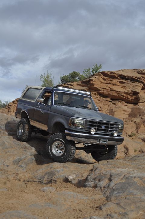 1991 Ford Bronco - This Ford Bronco navigates a challenging rocky trail under a cloudy sky.