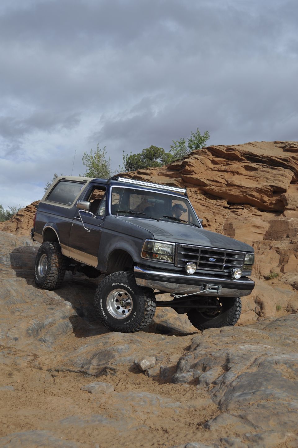 Dark gray Ford Bronco with lifted suspension and off-road tires climbing rocky terrain