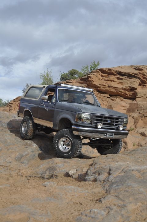 1991 Ford Bronco - This lifted Ford Bronco navigates a challenging rocky trail under a cloudy sky.