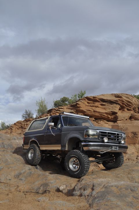 1991 Ford Bronco - A modified Ford Bronco navigates a rocky, off-road landscape under a cloudy sky.
