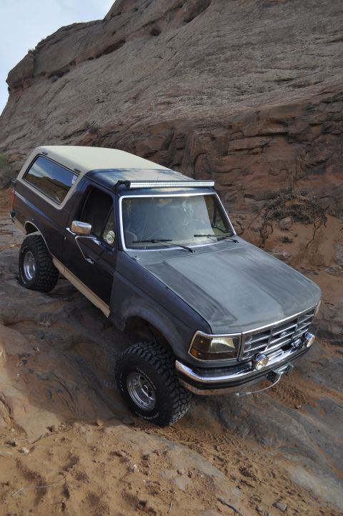 1991 Ford Bronco - This Ford Bronco is navigating a challenging off-road trail with steep, rocky inclines.