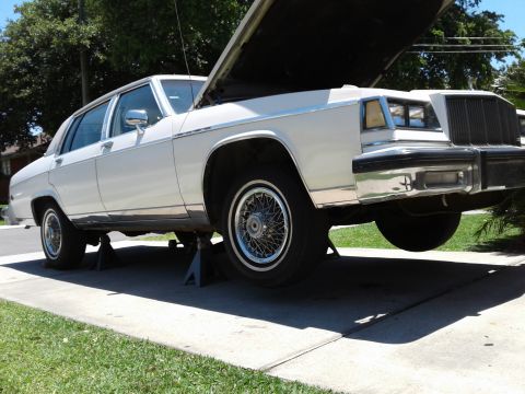 1984 Buick Electra - A white 1984 Buick Electra is shown on jack stands with its hood open, indicating maintenance or repair work.