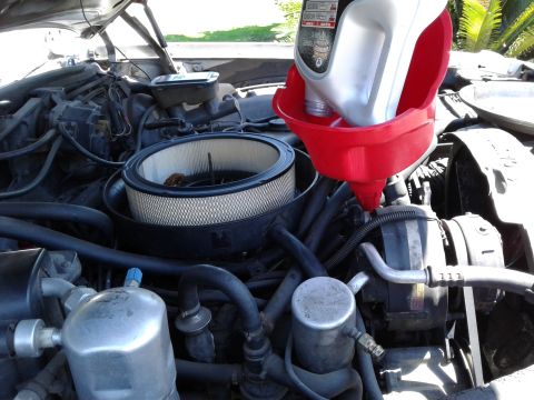 1984 Buick Electra - Pouring oil into the engine bay of a 1984 Buick Electra, showing the air filter and engine components.