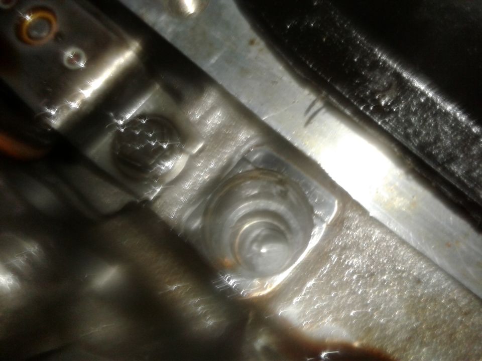 Close-up of a metal engine component with bolt holes and some rust