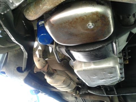 1984 Buick Electra - The underside of a vehicle reveals its engine oil pan, exhaust system, and a blue oil filter.