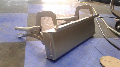 1985 Ford Bronco - A metal component is secured with clamps on a garage floor.