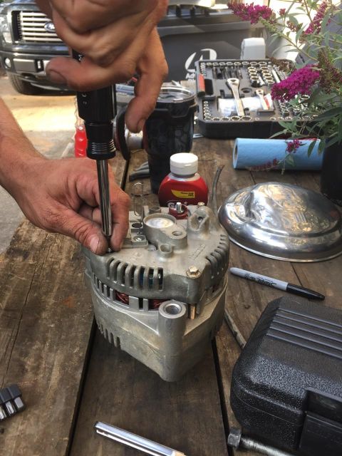 1988 Ford Bronco - A close-up view of an alternator being repaired, with various tools and a chrome hubcap visible on a rustic wooden surface.