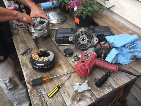 1988 Ford Bronco - Disassembled alternator components and various tools are laid out on a rustic wooden surface, suggesting a repair or rebuild process.