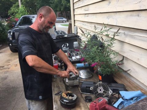 1988 Ford Bronco - Man repairs car alternator parts on a workbench outdoors, with a black Ford truck visible.