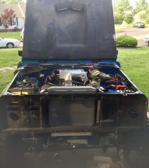 1974 Ford Bronco - The engine bay of a blue vehicle is exposed with the hood up, revealing the engine, radiator, and various wiring components.