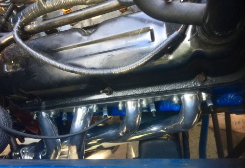 1974 Ford Bronco - Engine detail showing chrome exhaust headers and spark plugs, with visible wiring and engine block.