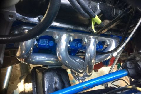 1974 Ford Bronco - Shiny exhaust headers and blue engine components are shown in this engine bay detail shot.