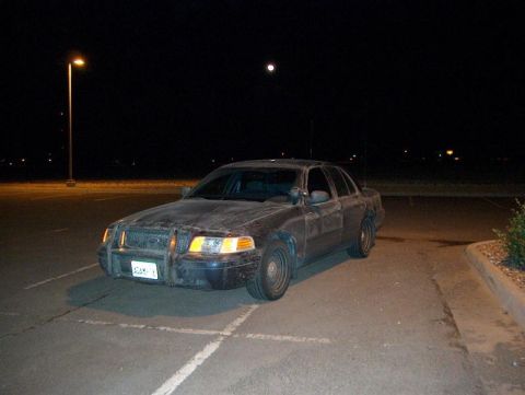 2001 Ford Crown Victoria - A dark 2001 Ford Crown Victoria, equipped with a push bar, is seen parked in a lot under the moonlight.