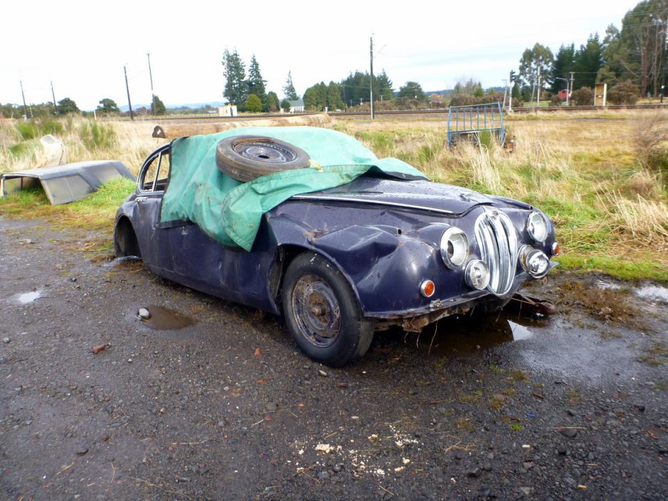 Dark blue sedan covered by a tarp with a spare tire on top, front view