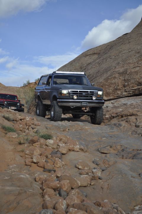 1991 Ford Bronco - Two off-road vehicles navigate a challenging rocky terrain under a partly cloudy sky.