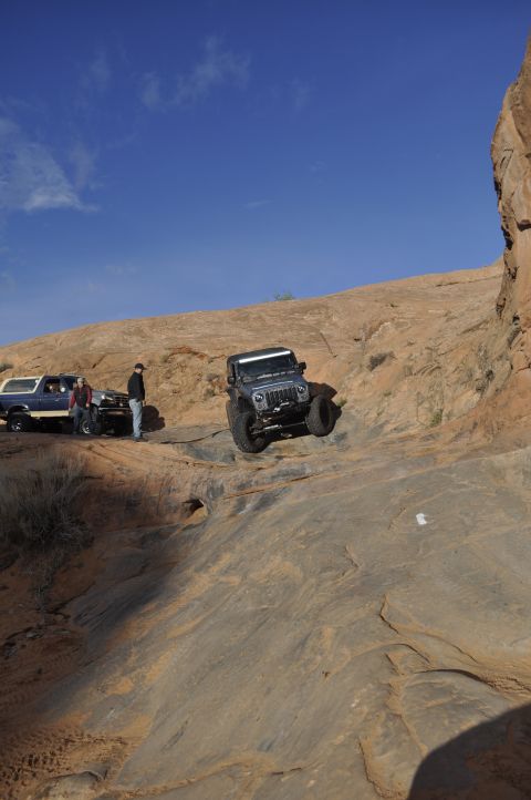 1991 Ford Bronco - Jeep Wrangler navigates a steep rocky incline in Moab, with a Ford Bronco and another SUV waiting on the trail.
