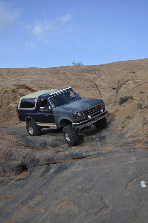 1991 Ford Bronco - This Ford Bronco is navigating a rocky incline under a clear blue sky.