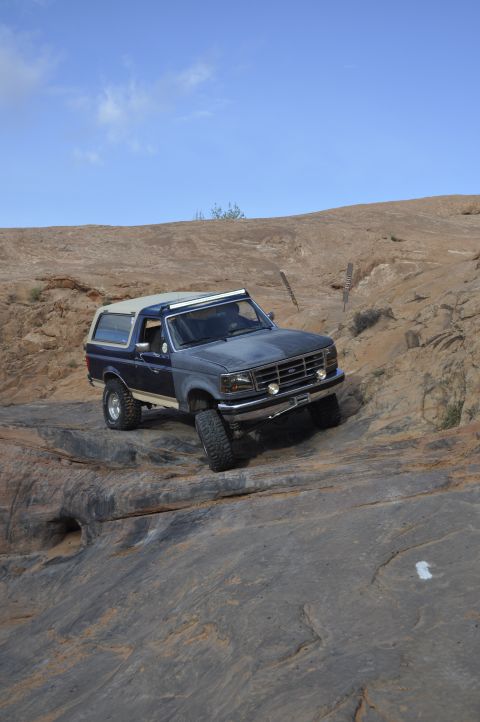 1991 Ford Bronco - Ford Bronco navigates a challenging rocky trail under a clear blue sky.