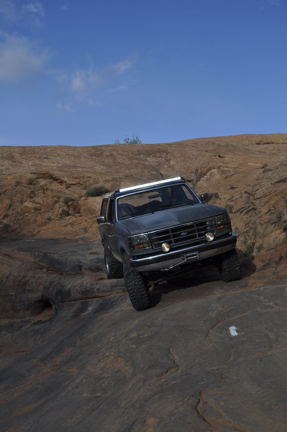 1991 Ford Bronco driving over rocky terrain with a light bar on the roof