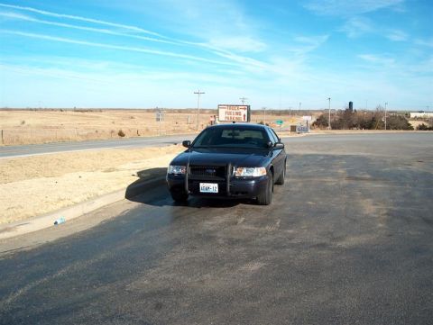 2001 Ford Crown Victoria - A black Ford Crown Victoria Police Interceptor is parked in a lot with a truck fueling station sign in the background.