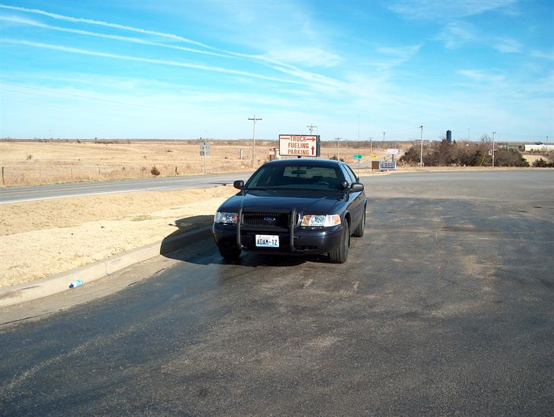 Black 2001 Ford Crown Victoria Police Interceptor parked in a lot, front view. License plate reads ADAM-12