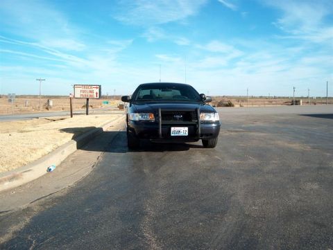 2001 Ford Crown Victoria - A black 2001 Ford Crown Victoria police car is parked in front of a truck fueling parking sign under a blue sky.