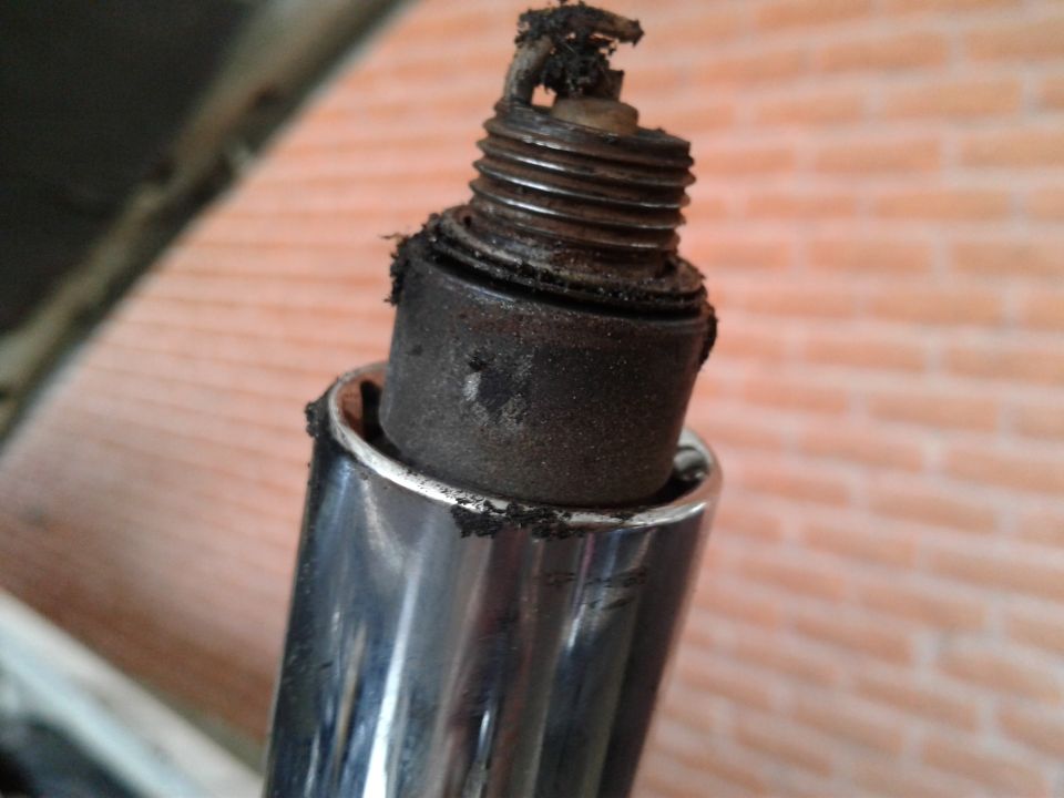 Heavily fouled spark plug with carbon buildup, removed from engine