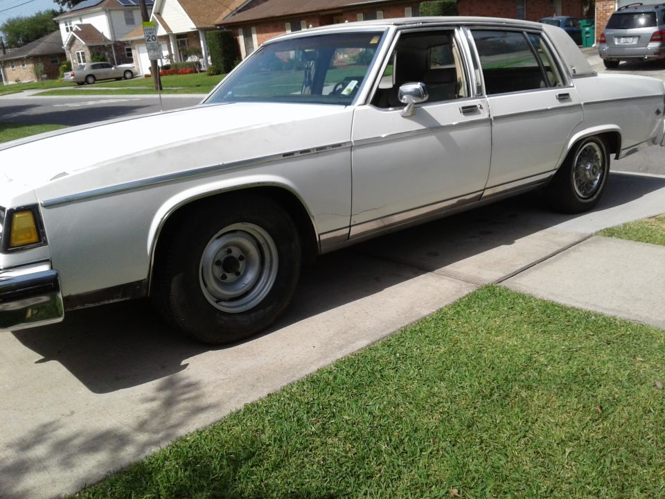 White four-door sedan parked on a driveway, showing side profile with chrome trim and vinyl roof.