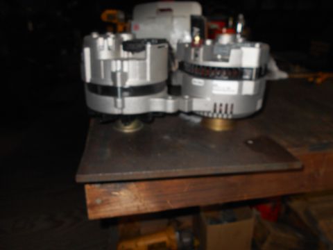 1992 Ford Bronco - Two silver alternators are mounted on a flat metal plate, which is resting on a wooden surface. The alternators appear to be identical and…