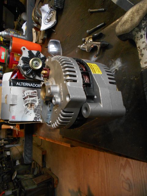 1992 Ford Bronco - A silver alternator is shown on a wooden workbench, partially obscuring a cardboard box labeled "ALTERNATOR". Other automotive parts and to…