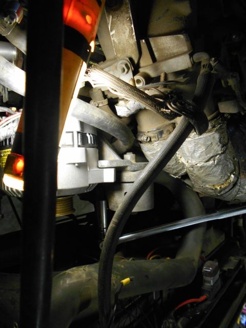 1992 Ford Bronco - A close-up view of automotive engine components, including an alternator, hoses, and wiring, illuminated by a bright light.