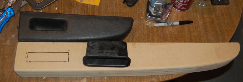 Car door handle trim piece on wood with drawn outline and tools in background.