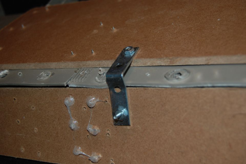 Metal bracket attached to brown surface with screws and glue.