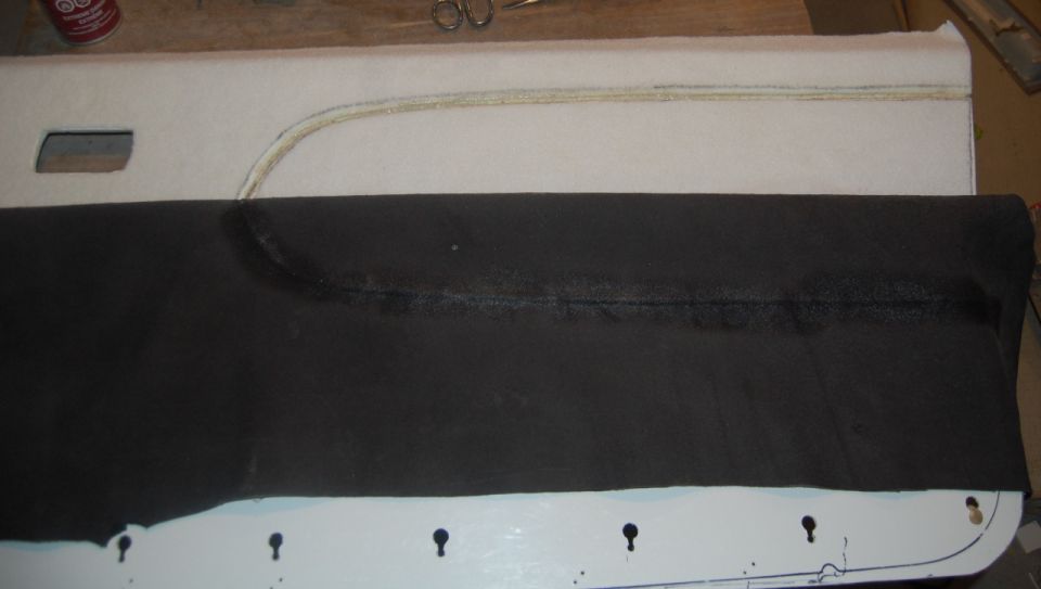 Car door panel upholstery with black fabric over padded section and door handle cut-out.