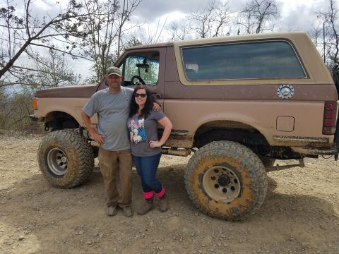 1988 Ford Bronco - A man and a woman stand in front of a lifted, two-tone brown 1988 Ford Bronco with large off-road tires. The vehicle appears to be on a dir…