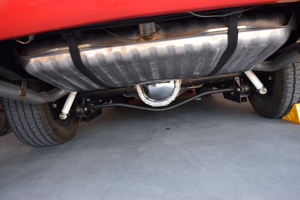 Underside view of a red vehicle's rear axle, fuel tank, and suspension.